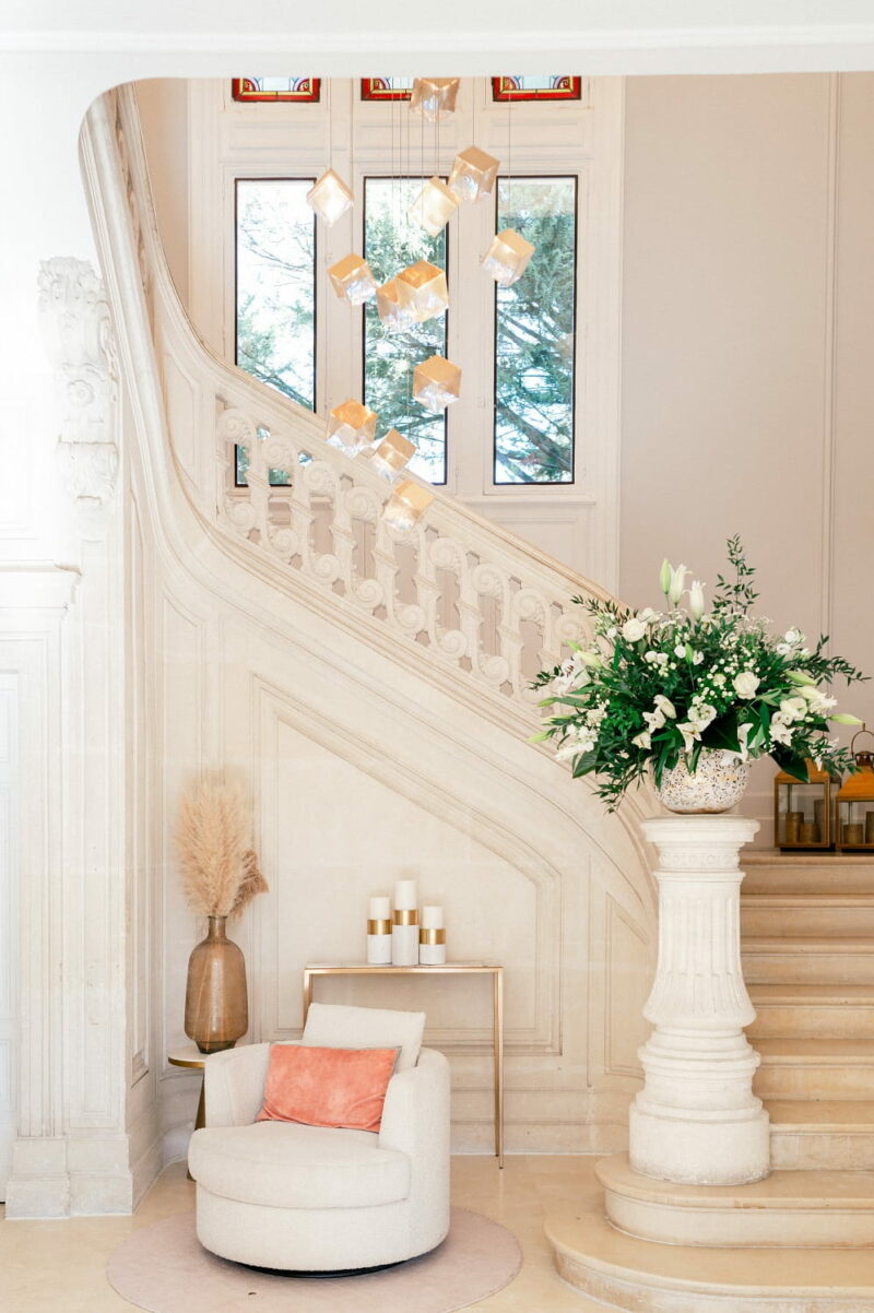 Hall et escalier du Château des Trois Fontaines avec composition florale et suspension lumineuse Hall et escalier du Château des Trois Fontaines - Raja Agency