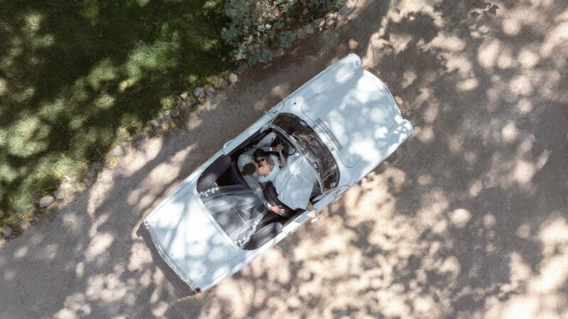 Couple de jeunes mariés allongés dans une voiture de luxe blanche, vue du dessus Couple de jeunes mariés allongés dans une voiture de luxe, vue drone - Raja Agency