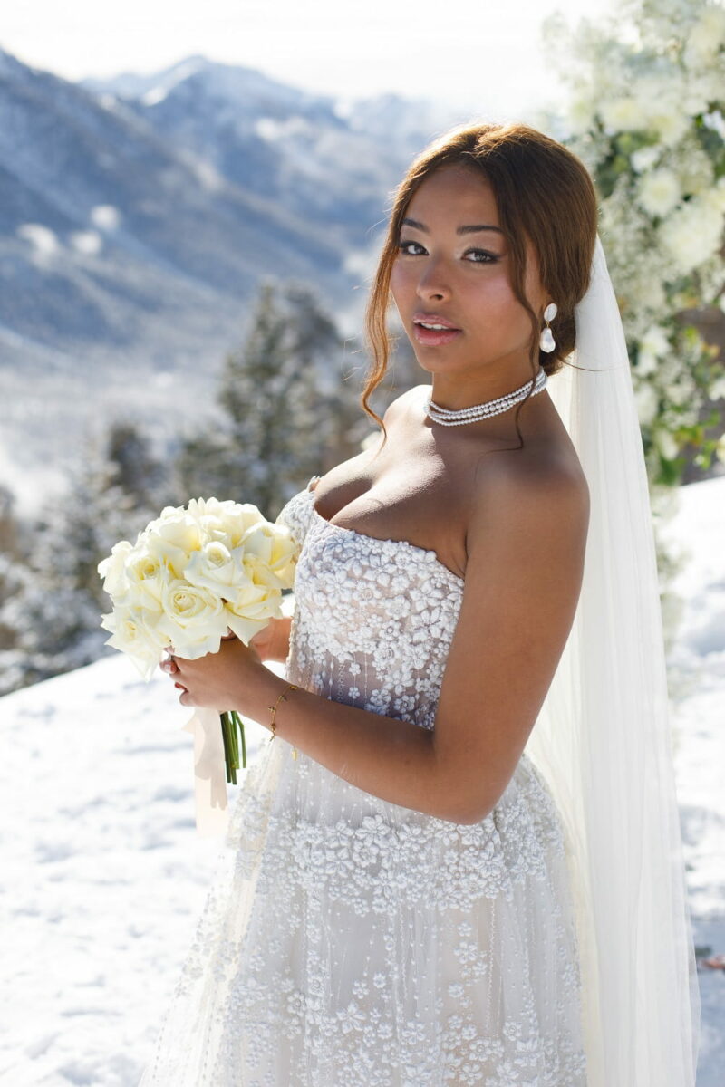Mariée tenant son bouquet à la main et regardant l'objectif, juste avant une cérémonie dans la neige Mariée tenant son bouquet à la main et regardant l'objectif - Raja Agency