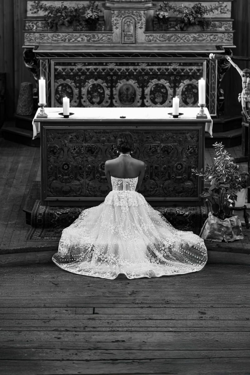 Mariée se tenant à genoux face à l'autel de l'église, sa traîne est étendue derrière elle Mariée se tenant à genoux face à l'autel de l'église - Raja Agency